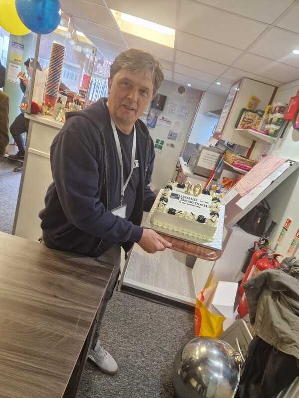 Image shows Daren Mountain, Manager of House in the Basement Youth Cafe holding a Cake to celebrate 10 years of House in the Basement Youth Cafe being open. 