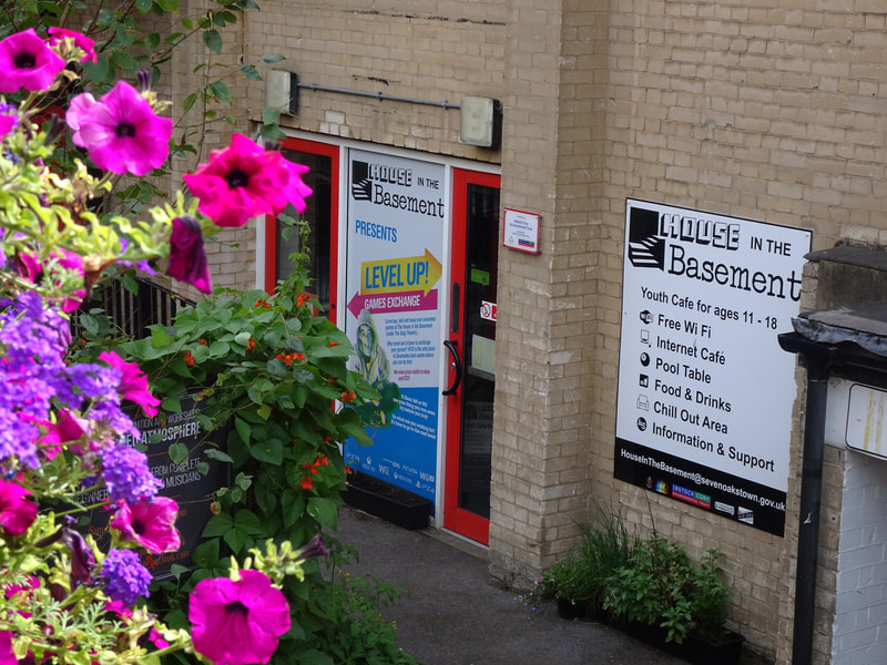image shows the entrance to House in the Basement Youth Cafe with flowers in the left side of the image. 